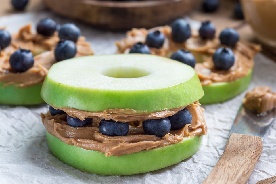 Sliced cored green apples layered with peanut butter and blueberries